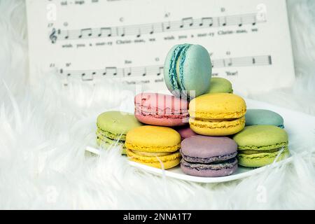Farbenfrohe Makronen auf weißem quadratischem Teller und flauschigem Pelz mit Hintergrundmusik aus Weihnachtsblättern Stockfoto