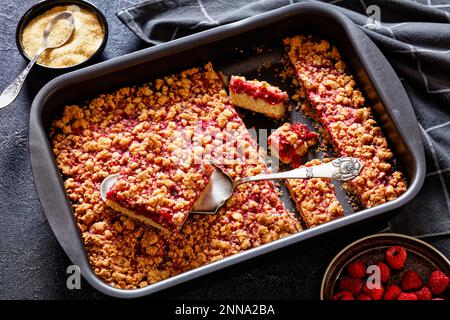 Himbeerstäbchen in Backform auf Betontisch mit Kuchenschaufel und Zutaten Stockfoto