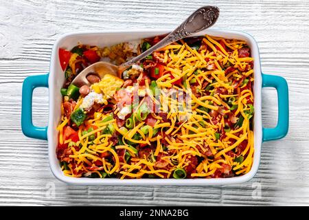 pinto Beans Speck Maisbrotsalat mit Tomaten, Paprika, Mais und Cheddar Käse in rechteckiger Schüssel auf weißem Holztisch mit Löffel, horizontale Ansicht Stockfoto