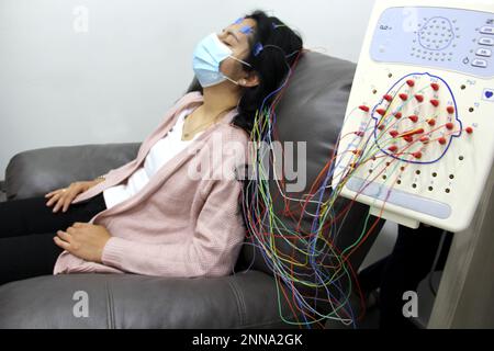 Lateinische Frau mit Schutzmaske in medizinischen Tests, Elektroenzephalogramm und Hirnkartierung in Zeiten der Covid-19-Kontingenz Stockfoto