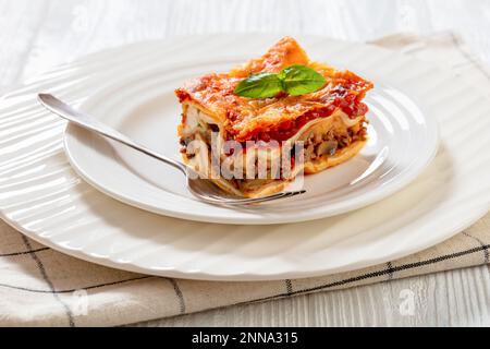 Lasagna mit Ricotta-Käse, Rinderhack, Pilzen, Zucchini und Tomatensoße auf weißem Teller mit Gabel Stockfoto