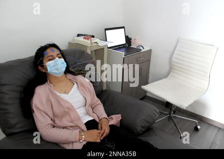 Lateinische Frau mit Schutzmaske in medizinischen Tests, Elektroenzephalogramm und Hirnkartierung in Zeiten der Covid-19-Kontingenz Stockfoto