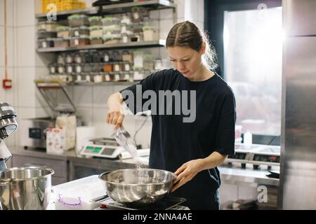 Eine Köchin arbeitet in einer modernen Industrieküche. Der Vorgang der Zubereitung von Kuchen in einer Bäckerei oder einem Café. Stockfoto