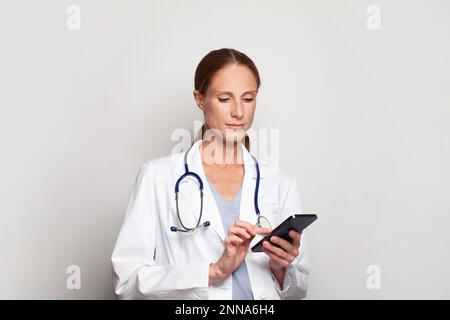 Medizin, Technologie und Gesundheitskonzept. Erfolgreiche attraktive mittelErwachsene Ärztin oder Krankenschwester hält Smartphone in der Hand Stockfoto
