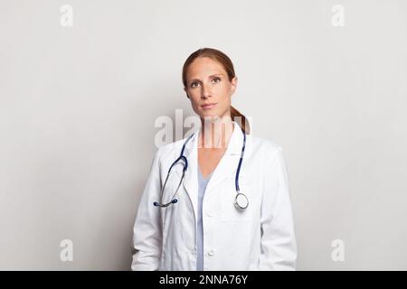 Sehr freundlicher Arzt oder Krankenschwester mit Stethoskop in weißem Laborkittel, der drinnen steht Stockfoto