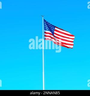 Die große Nationalflagge der Vereinigten Staaten flattert im Wind an einem klaren, sonnigen Tag. Leuchtendes und lebendiges Stolz- und Einheitskonzept. Stockfoto