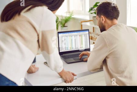 Männliche und weibliche Kollegen prüfen die Tabelle auf dem Laptop-Bildschirm Stockfoto