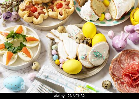 Festliches Abendessen, Osterbrunch. Ostertisch mit einer Auswahl an Backwaren, Desserts, gefüllten Eiern und gefärbten Eiern auf Marmorhintergrund. Stockfoto