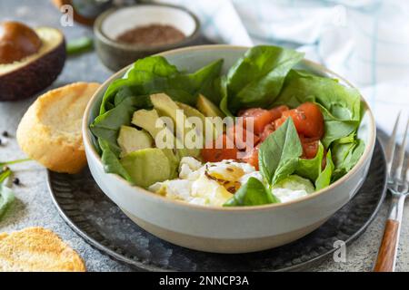 Klassisches Frühstück, Brunch - mit pochiertem Ei, Avocado, Rucola, Leinsamen und gesalzenem Lachs auf grauem Hintergrund. Stockfoto