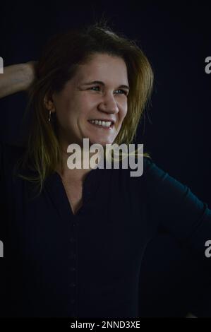 Porträt einer schönen blonden Frau, die fröhlich lacht und ihr Haar hinter dem Kopf hält Stockfoto