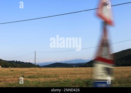 Die Berge in der Ferne blockieren den Horizont. Vor einer Ebene und direkt im Vordergrund sind Wegweiser am Straßenrand durch Schnelligkeit verschwommen Stockfoto