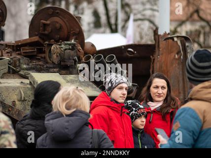 Mutter mit Söhnen, die ein Foto in der Nähe eines verbrannten und geschmolzenen rostigen Wrackwerks eines russischen Panzers T72B machen, der während der russischen Invasion der Ukraine zerstört wurde Stockfoto