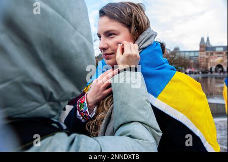 Während der Demonstration sieht man eine Frau, die die Farben der Ukraine an eine andere malt. In Amsterdam Tausende ukrainische Menschen und Anhänger gingen vom Museumplein zum Dam-Platz, um die niederländische Gesellschaft daran zu erinnern, dass der Krieg weitergeht und dass mutige ukrainische Menschen ihr Land verteidigen und dass die Ukraine damit Unterstützung braucht.denn Freitag, der 24. Februar, ist ein Jahr, seit Russland seine Existenz begonnen hat Krieg gegen die Ukraine, mehrere Demonstrationen sind in den Niederlanden geplant. Mehr als acht Millionen Menschen wurden gezwungen, die Ukraine zu verlassen, und weitere fünf Millionen waren im Inland Stockfoto