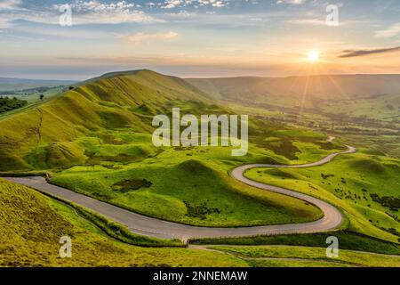Lange gewundene Landstraße, die durch die ländliche Landschaft im English Peak District führt, mit wunderschönem Abendsonnenlicht. Stockfoto