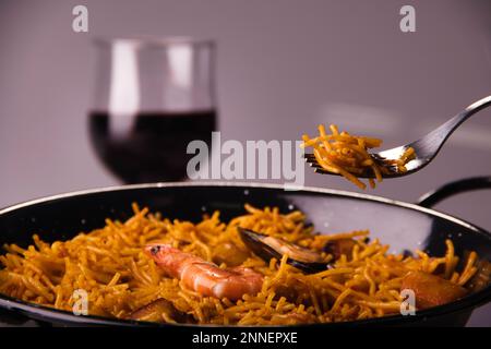 Nahaufnahme eines Tellers Fideua serviert mit einem Glas Rotwein Stockfoto