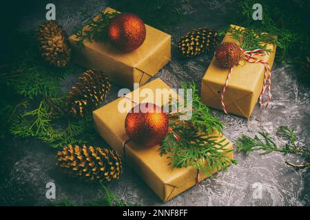 Craft Paper präsentiert Kartons Cord Fir Tree Branch Rote Kugeln auf Betonhintergrund. Weihnachtsgeschenkkonzept, Draufsicht. Analoge Kamera Antique Toned Image (Analoges Tonbild). Stockfoto