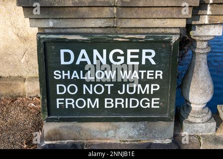 Gefahr. Flachwasser. Springen Sie nicht von der Brücke. Warnschild auf der Serpentine Bridge, die Hyde Park und Kensington Gardens in London, England, teilt. Stockfoto