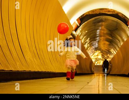 Die ganze Länge eines Mädchens, das Ballons hält, während es im Tunnel läuft Stockfoto