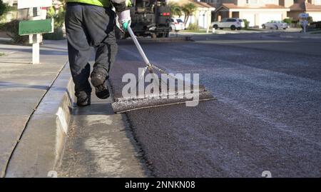 Nahaufnahme der Füße und Werkzeuge des Arbeiters, die die frische Schlammdichtung glätten Stockfoto