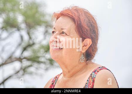 Porträt einer selbstbewussten, erwachsenen Frau, die im Freien lächelt und etwas nach oben in einer positiven Einstellung schaut. Stockfoto