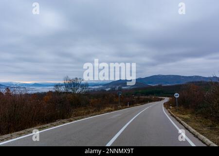 Eine atemberaubende Berglandschaft mit einer Asphaltstraße mit schneebedeckten Gipfeln, die sich über den Wolken erheben Stockfoto