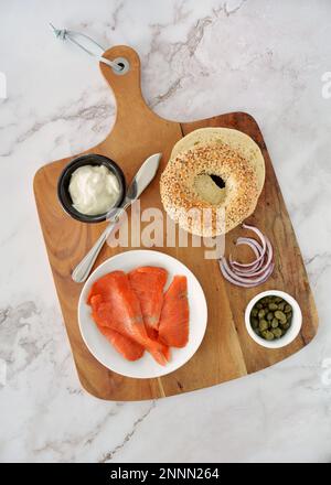 Zutaten für geräucherte Lachsbaget in flacher Lagenzusammensetzung. Lebhafter geräucherter Lachs, Sesammohn-Bagel, Kapern, Schlagsahne und rote Oni Stockfoto