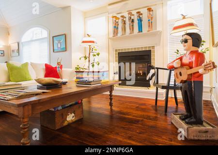Couchtisch aus Kiefernholz im antiken Stil, weißes Polstersofa mit grünen und roten Velours-Kissen, Elvis Folk Art Skulptur, Kamin im Wohnzimmer. Stockfoto