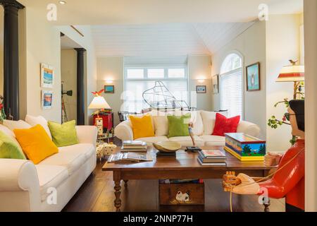 Couchtisch aus Kiefernholz im antiken Stil, weiße Polstersofas mit grünen, gelben und roten Velours-Kissen, Elvis Folk Art Skulptur im Wohnzimmer. Stockfoto