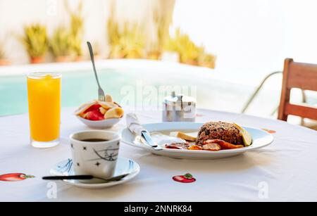 Nahaufnahme eines traditionellen Frühstücks auf einem Tisch mit Swimmingpool im Hintergrund. Frühstück auf dem Tisch in der Nähe des Swimmingpools Stockfoto