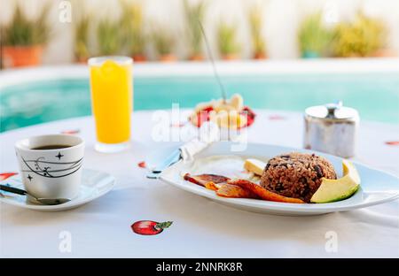 Frühstück auf dem Tisch in der Nähe des Swimmingpools. Nahaufnahme eines traditionellen Frühstücks auf einem Tisch mit Swimmingpool im Hintergrund Stockfoto