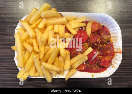 currywurst: Typisch deutsches Fast-Food-Gericht mit Schweinewürstchen, Curry-Ketchup-Sauce und pommes frites Stockfoto