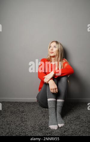 Gelangweilte junge Frau, die während der Quarantäne oder Selbstisolierung zu Hause bleibt und an der Decke anstarrt - grauer Hintergrund mit Kopierraum Stockfoto