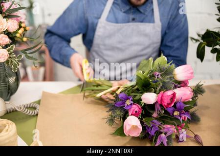 Nahaufnahme männlicher Florist, der Papier schneidet, Blumenstrauß verpackt. Schönes Foto Stockfoto