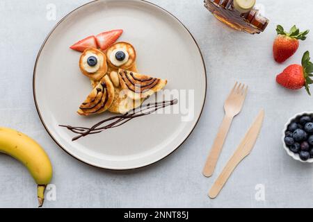 Von oben aus haben Sie einen Blick auf Pfannkuchen in Form einer Eule, serviert mit Sirup und Obst. Stockfoto