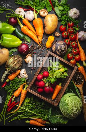 Rettich und Karotten frisch gebrüht in alter Holzbox und frisches Bio-Gemüse auf rustikalem schwarzem Betonhintergrund. Herbsternte, vegetarisch Stockfoto