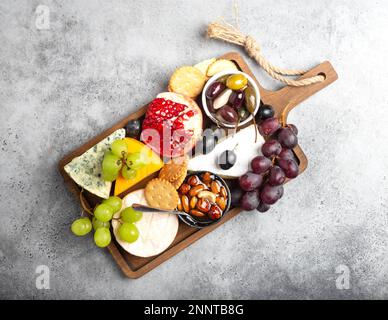 Auswahl an Käse und Vorspeisen, Camembert, Brie, Cheddar, Cracker, Trauben, Nüsse, Honig. Gemischte Käsemischung auf rustikalem Holzbrett über Grau Stockfoto