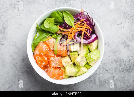 Blick von oben auf eine Schüssel mit frischem rohem Lachs, Avocado, Reis, Spinat, Gemüse. Traditionelles hawaiianisches Gericht auf rustikalem Steinhintergrund. Gesund und Stockfoto