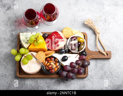 Auswahl an Käse und Vorspeisen, Rotwein, Camembert, Brie, Cheddar, cracker, Trauben, Nüsse, Honig. Gemischter Käse auf rustikalem Holzbrett Stockfoto