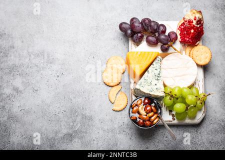 Auswahl an Käse und Vorspeisen, Camembert, Brie, Cheddar, Brot, cracker, Trauben, Nüsse, Honig. Gemischter Käse auf rustikalem Holzbrett mit Stockfoto