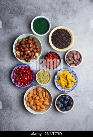 Set aus verschiedenen Superfoods in Schüsseln auf steingrauem Hintergrund: spirulina, Goji-Beere, Kakao, Matcha-Grüntee-Pulver, Quinoa, Chiasamen Stockfoto