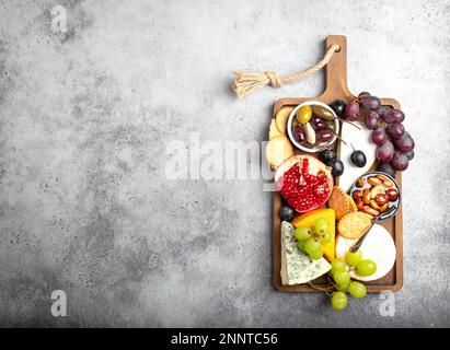 Auswahl an Käse und Vorspeisen, Camembert, Brie, Cheddar, Brot, cracker, Trauben, Nüsse, Honig. Gemischter Käse auf rustikalem Holzbrett mit Stockfoto