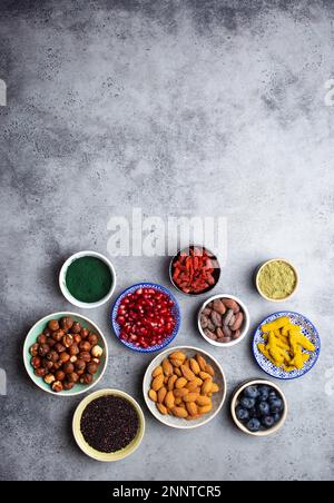 Verschiedene Superfoods in Schüsseln auf steingrauem Hintergrund: spirulina, Goji-Beere, Kakao, Matcha-Grüntee, Quinoa, chiasamen, Blaubeeren, Nüsse Stockfoto