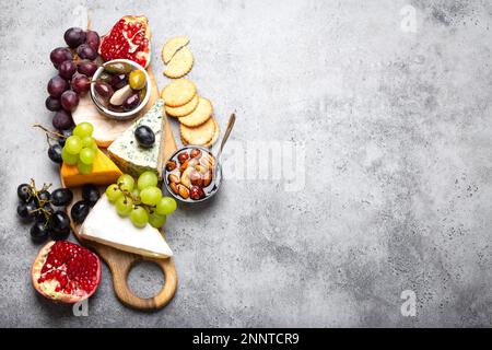 Auswahl an Käse und Vorspeisen, Camembert, Brie, Cheddar, Brot, cracker, Trauben, Nüsse, Honig. Gemischter Käse auf rustikalem Holzbrett mit Stockfoto
