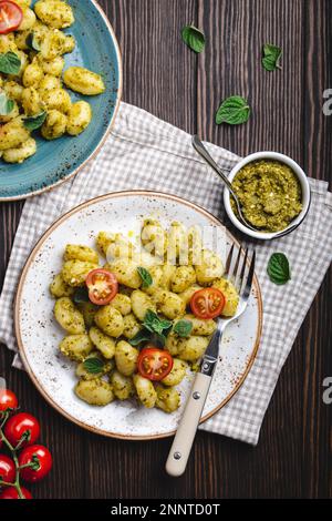 Gnocchi in Tellern mit grüner Pesto-Sauce, Tomaten und Kräutern auf rustikalem Holzhintergrund, Nahaufnahme, Draufsicht. Traditionelles italienisches Gericht Stockfoto