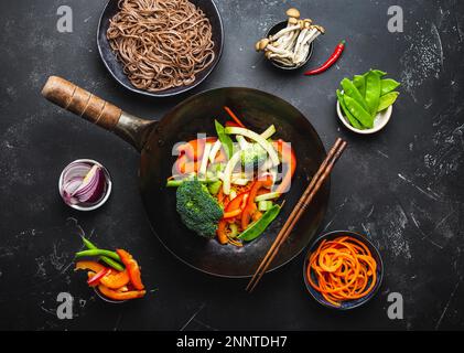 Zutaten für die Zubereitung von gebratenen Nudeln Soba. Schneiden Sie frisches Gemüse in der Wok-Pfanne, gekochte Soba-Nudeln in der Schüssel mit Stäbchen zum Kochen, schwarz Stockfoto