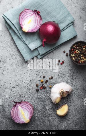Nahaufnahme, Draufsicht von geschnittenen rohen roten Zwiebeln, Knoblauch und Gewürzen auf rustikalem grauen Steinhintergrund. Kochen, vegetarisches Essen oder gesundes Essen Stockfoto