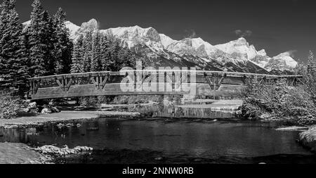 Fußgängerbrücke über den Policemans Creek in schneeweißer Landschaft mit Mount Rundle, Canmore, Alberta, Kanada Stockfoto