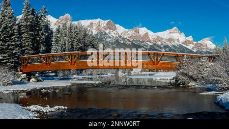 Fußgängerbrücke über Policemans Creek in einer verschneiten Berglandschaft mit Mount Rundle, Canmore, Alberta, Kanada Stockfoto