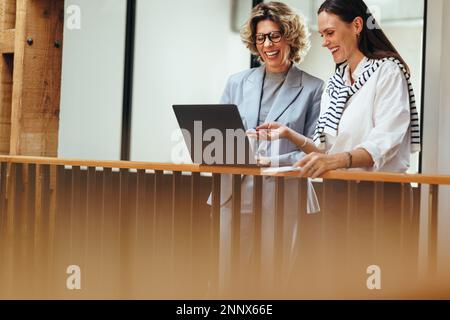 Professionelle Frauen kommunizieren mit ihrem Team per Videoanruf. Glückliche Geschäftsfrauen, die an einem virtuellen Meeting mit einem Laptop teilnehmen, lächeln, während sie über sich reden Stockfoto