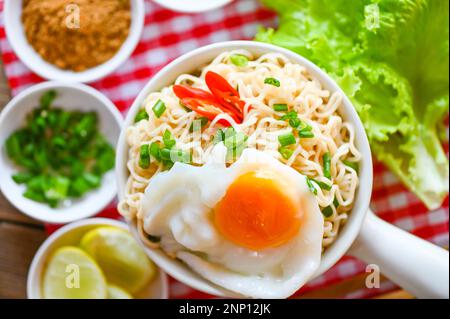 Nudelschüssel mit gekochtem Ei, Gemüse, Frühlingszwiebeln, Zitronensellerie, Salatsalat und Chili auf dem Tisch, Instant-Nudeln, die köstlich kochen und mit Schüssel essen Stockfoto